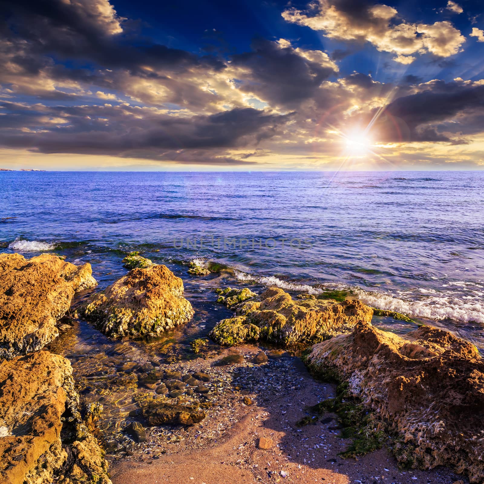 sea wave attacks the boulders and is broken about them at sunset