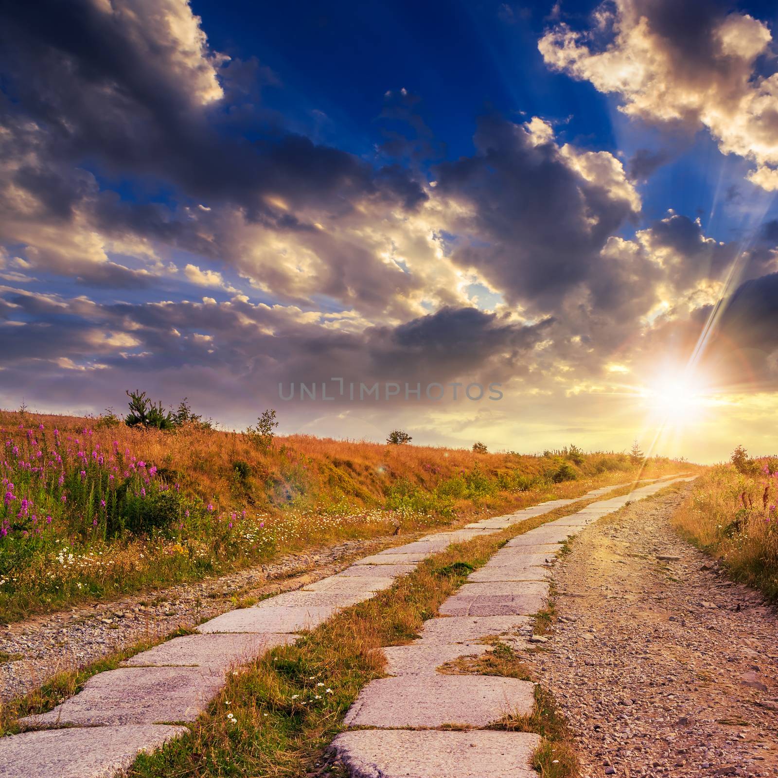 road of concrete slabs through the field turns uphill to the sky at sunset