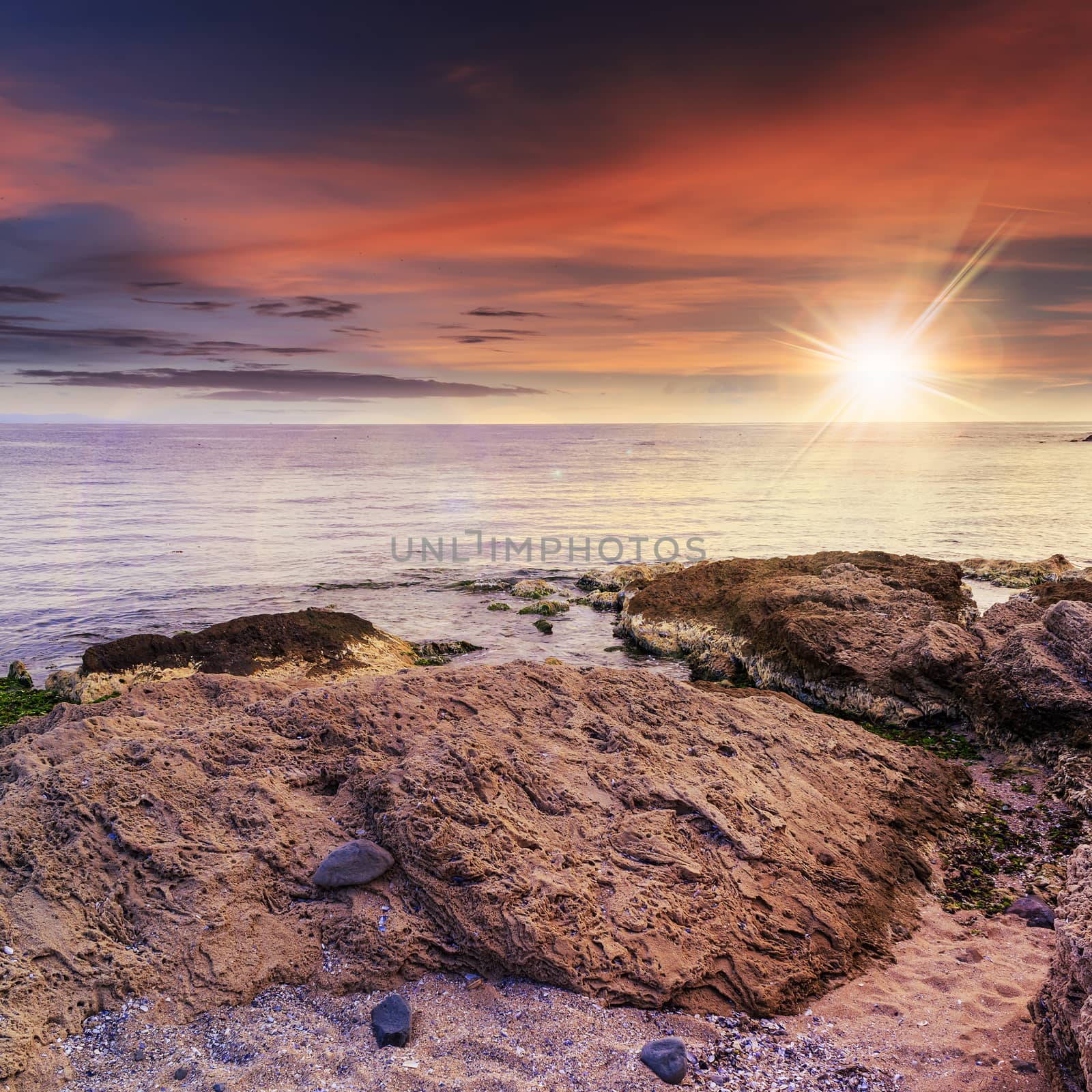 sea wave attacks the boulders and is broken about them at sunset