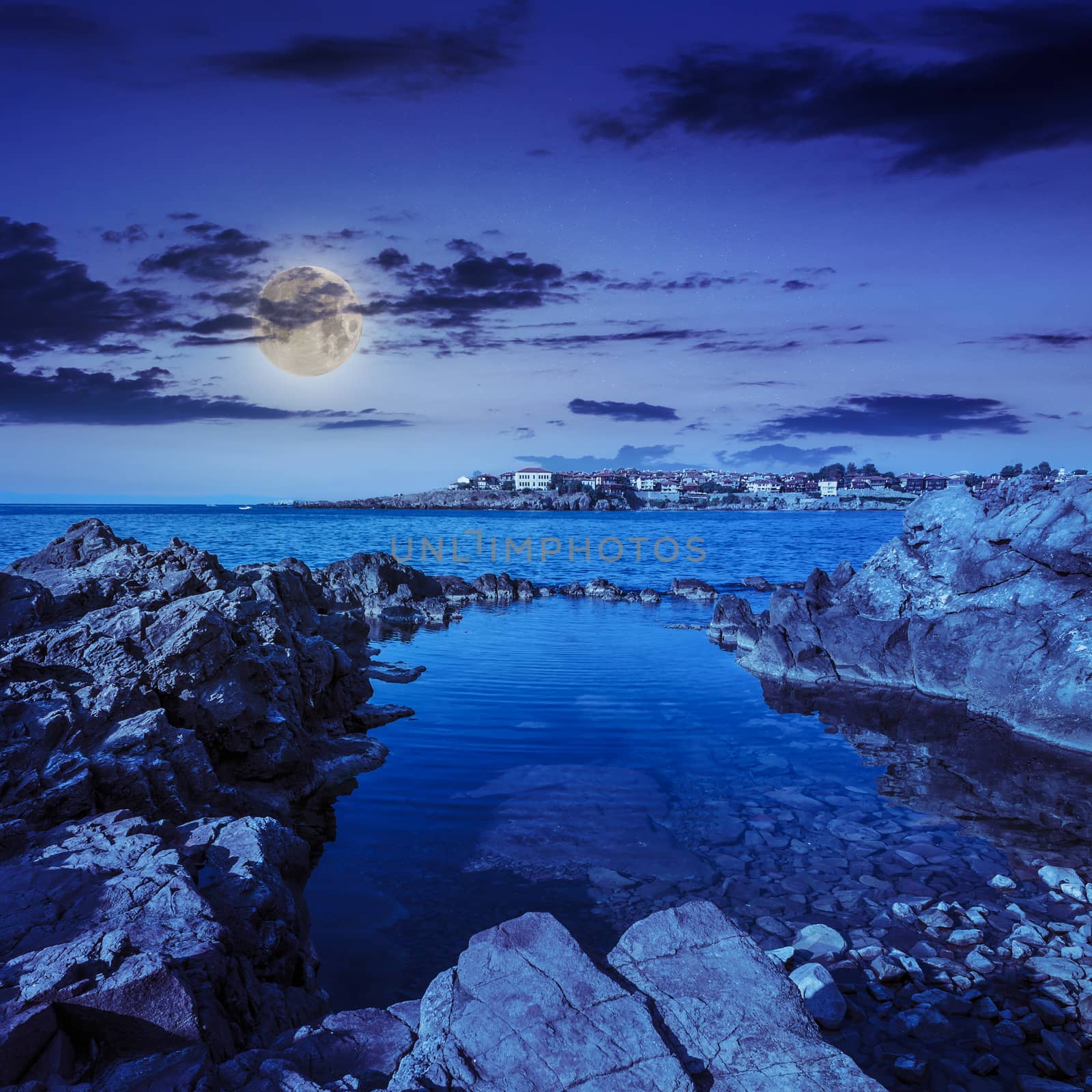 sea coast  with giant boulders against the old city at night in moon light