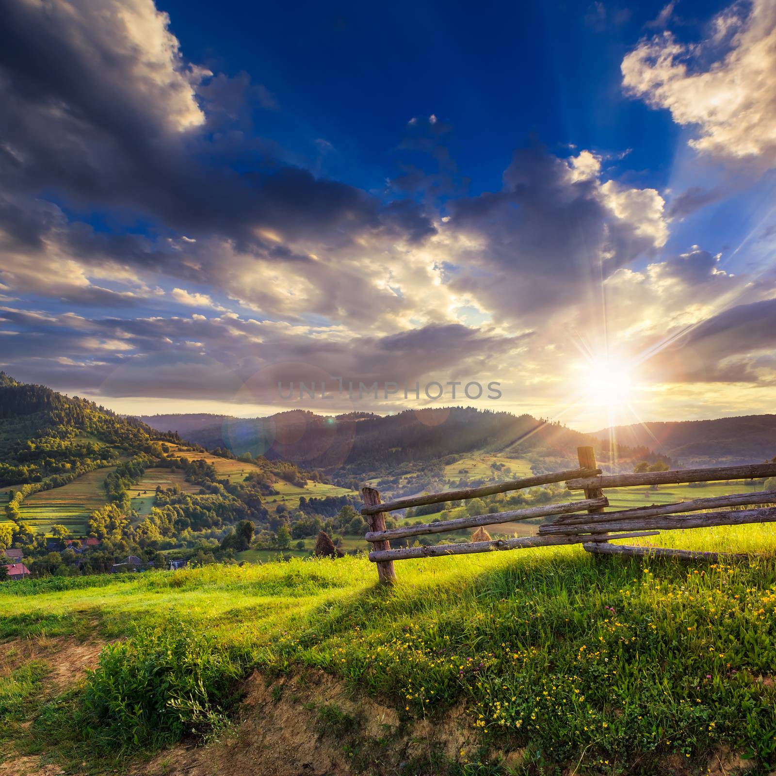 wooden fence in the grass on the hillside near the village at sunset