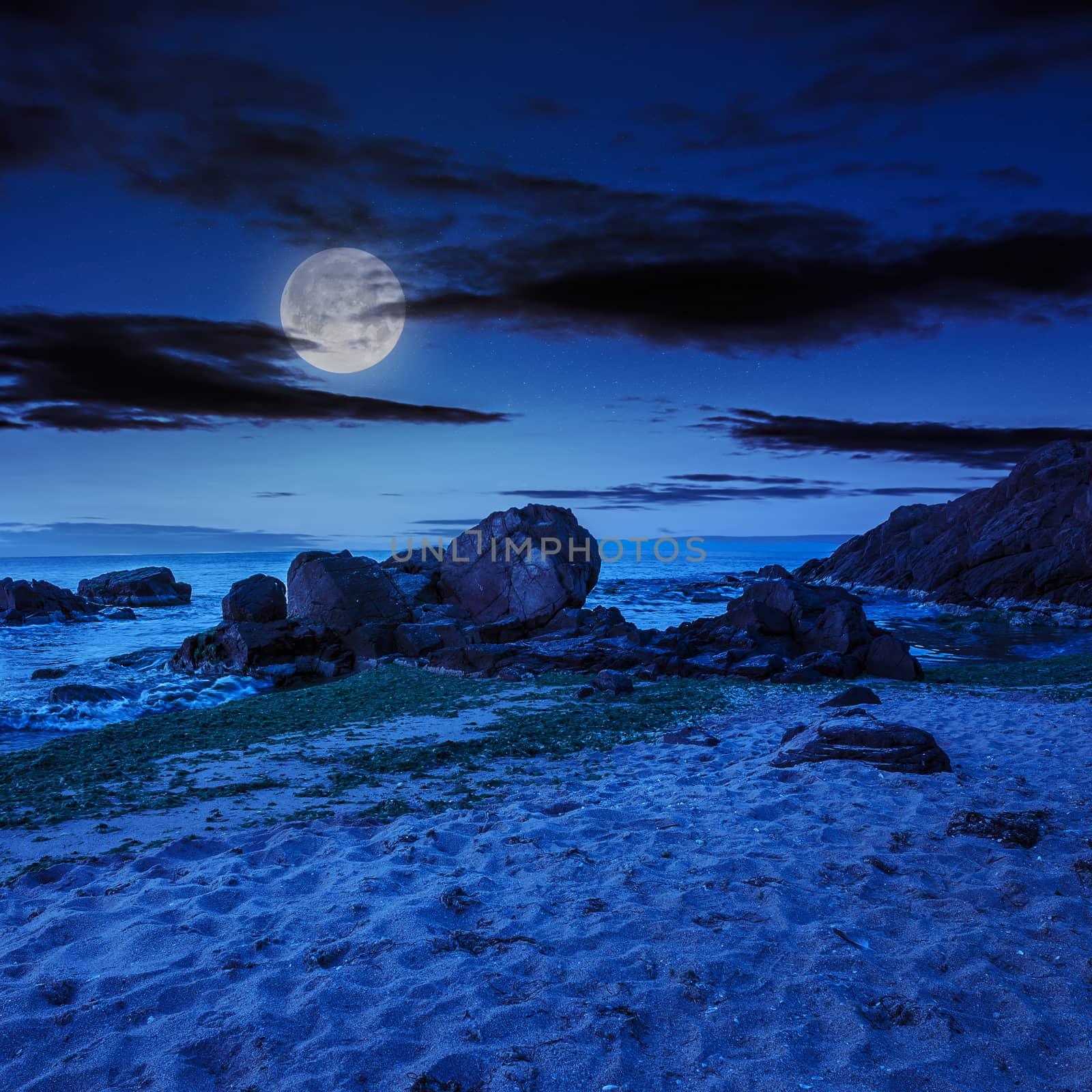 sea wave attacks the boulders and is broken about them at night in moon light