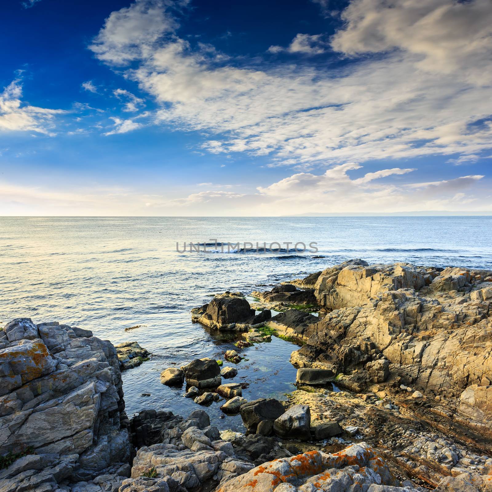 calm sea with fiev waves on coast with  boulders and seaweed