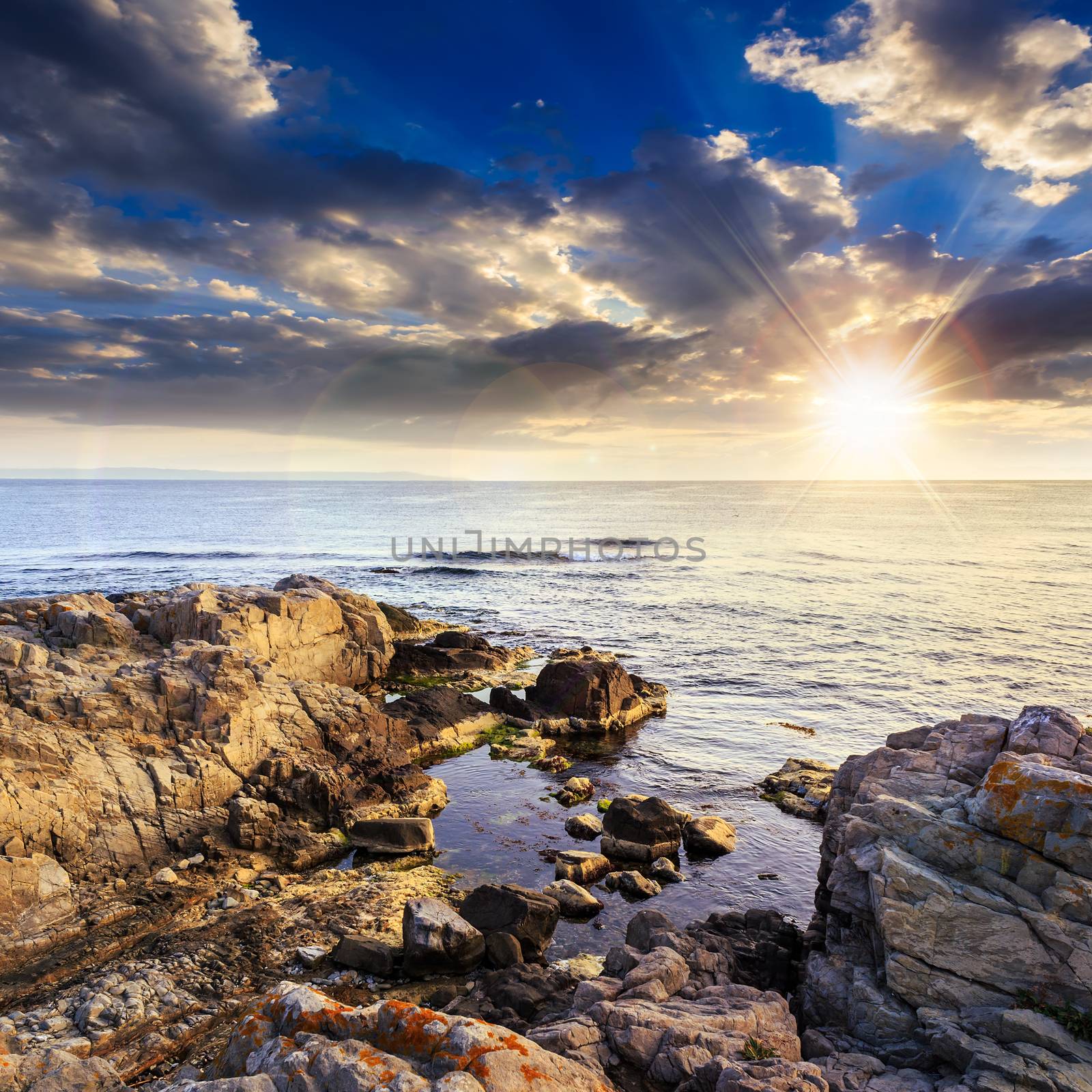 calm sea with fiev waves on coast with  boulders and seaweed at sunset