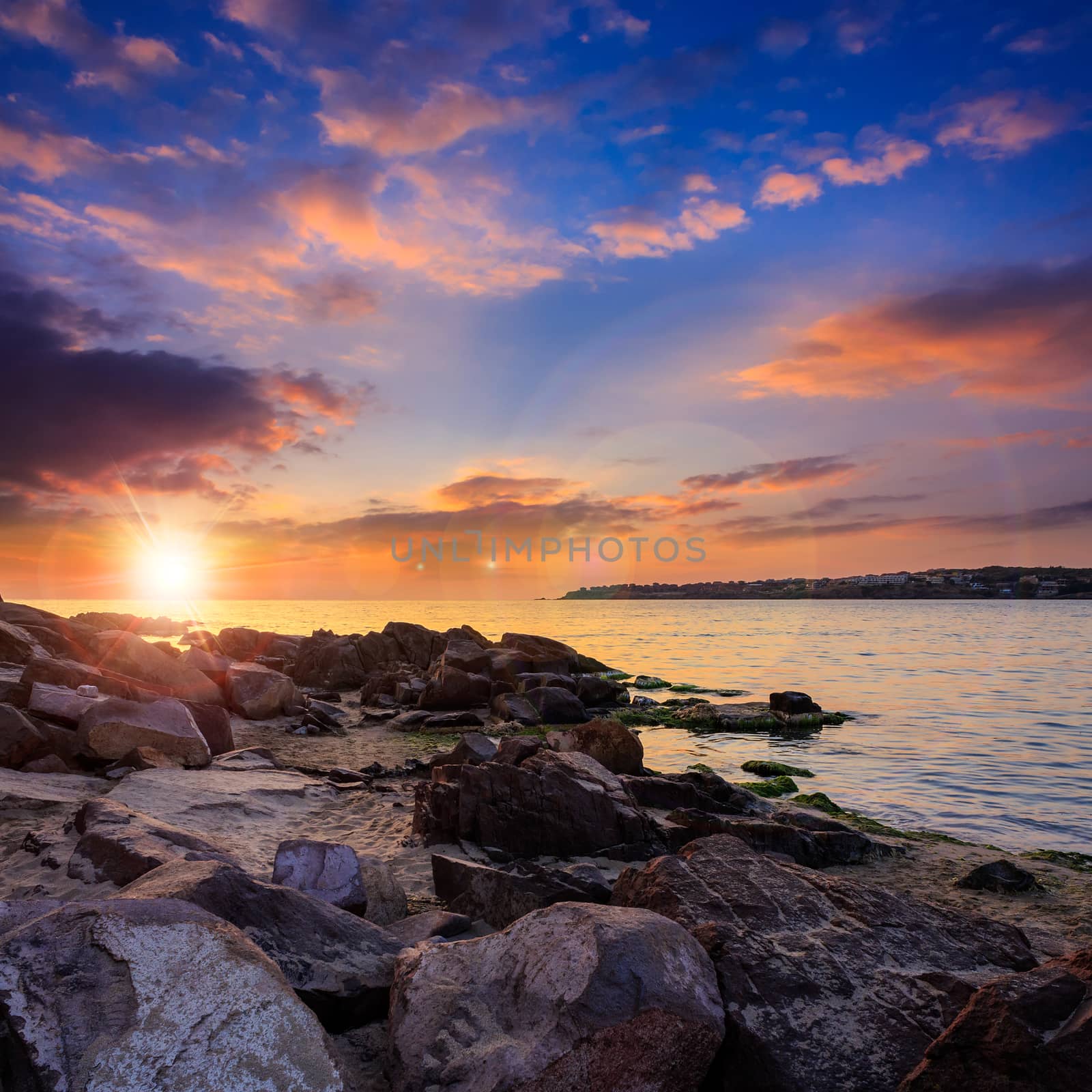 calm sea wave touches  boulders on rocky shore at bright hot sunrise