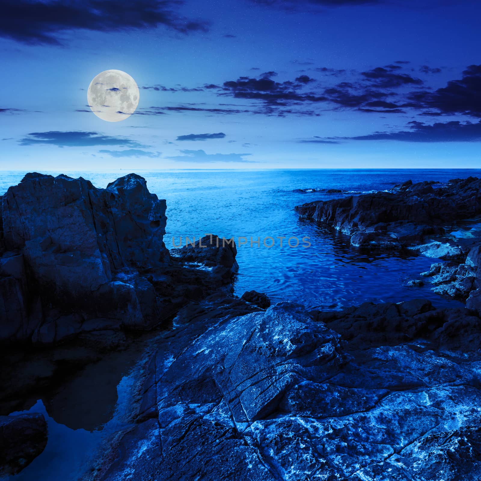 calm sea wave touch giant boulders on rocky shore at night in moon light