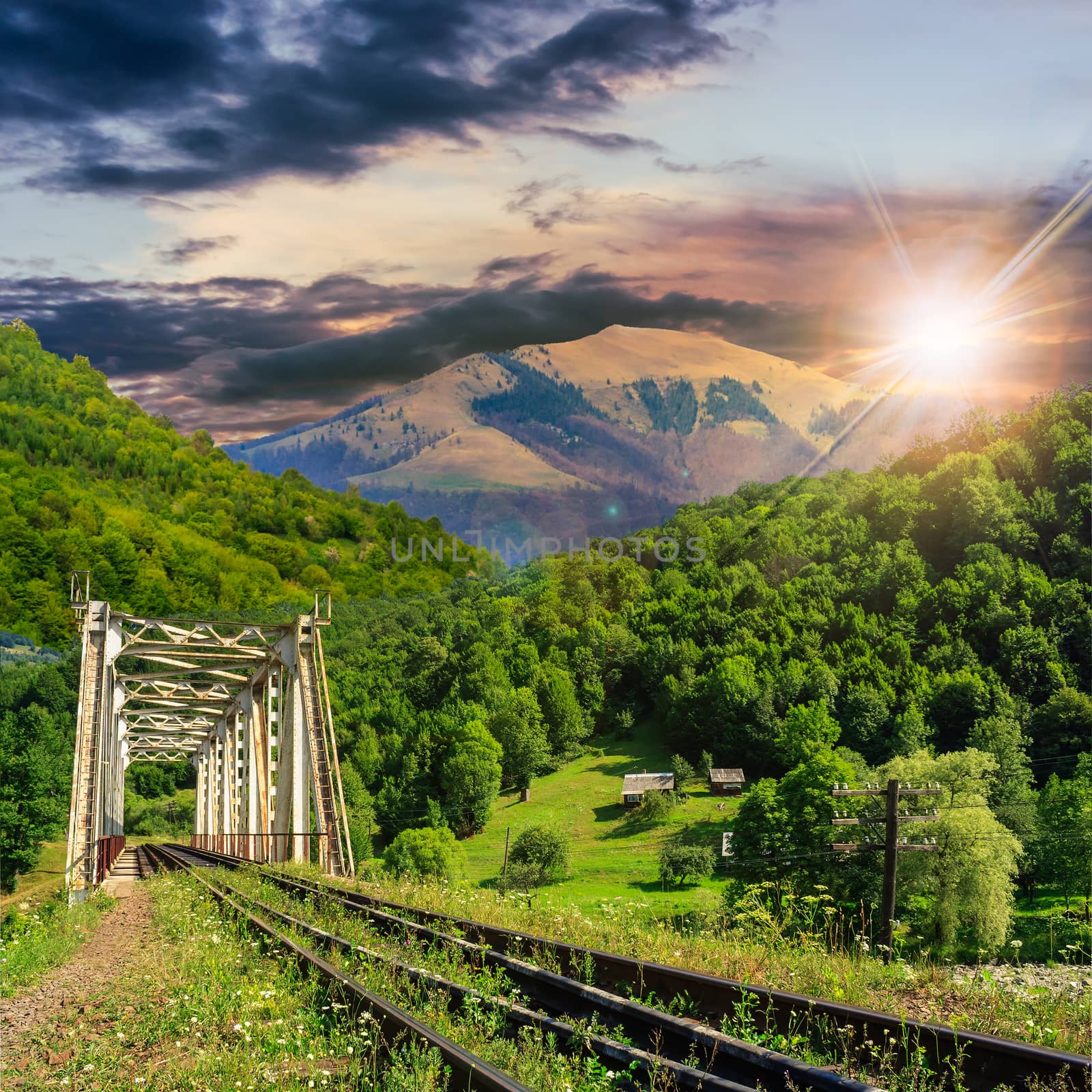 old railroad passes through the metal bridge in the mountain village at sunset