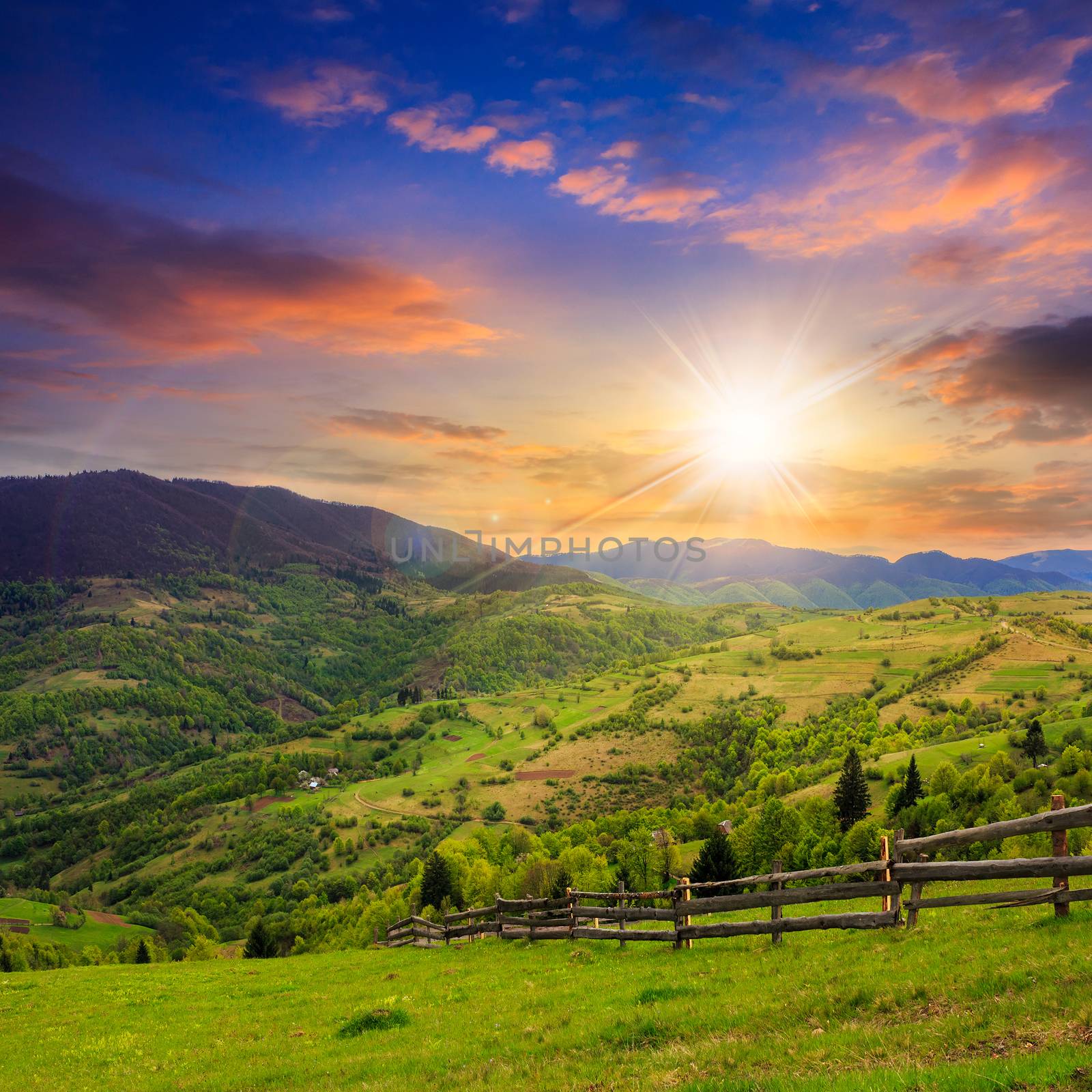 summer landscape. fence near the meadow on hillside. forest in fog on the mountain at sunset