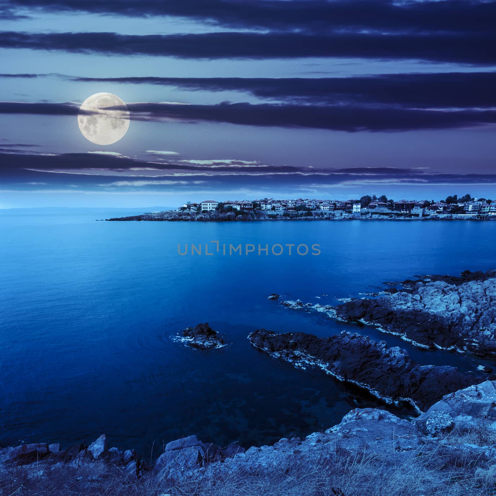 ancient city on a rocky shore near sea at night by Pellinni