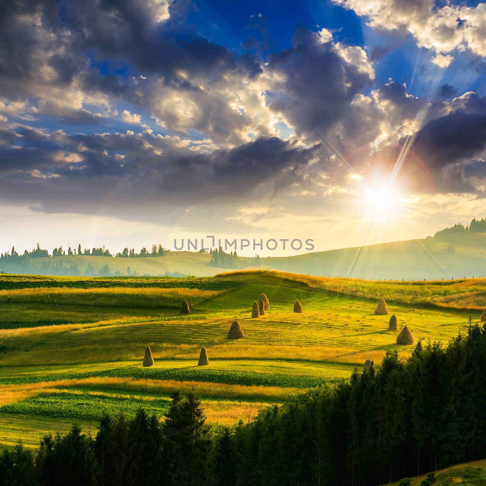 Stack of hay on a green meadow in the mountains at sunset under a blue summer sky