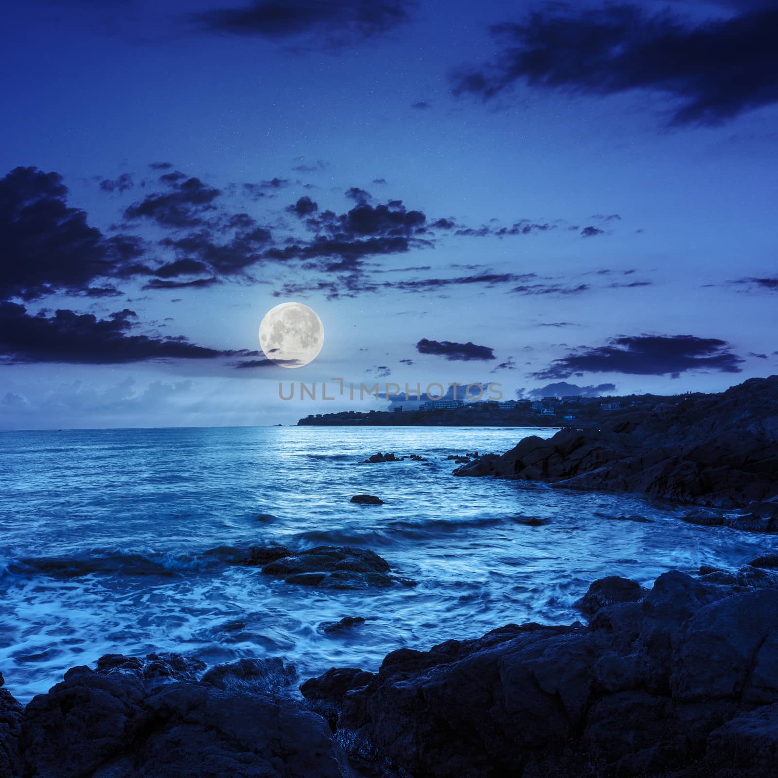 sea wave attacks the boulders and is broken about them at night in moon light