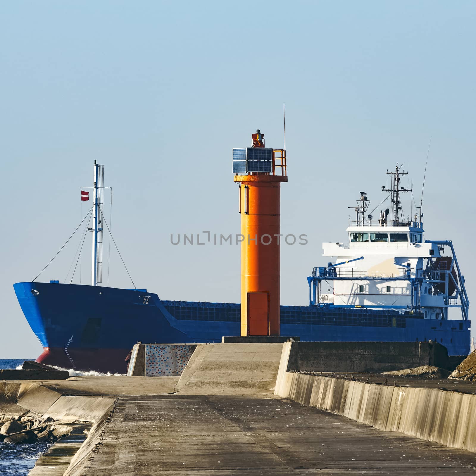 Blue cargo ship sailing against the breakwater dam