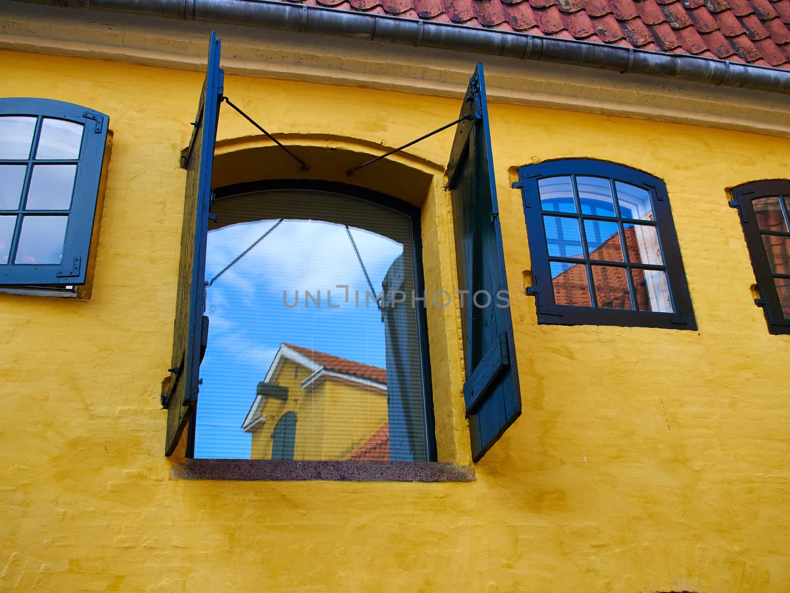 Rustic window with wooden exterior shutters on a yellow painted wall
