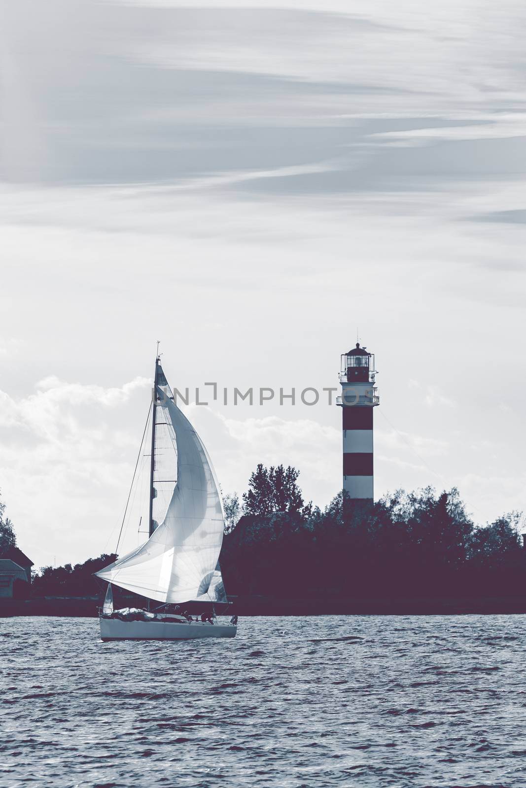 Sailboat moving past the big lighthouse in evening, Latvia