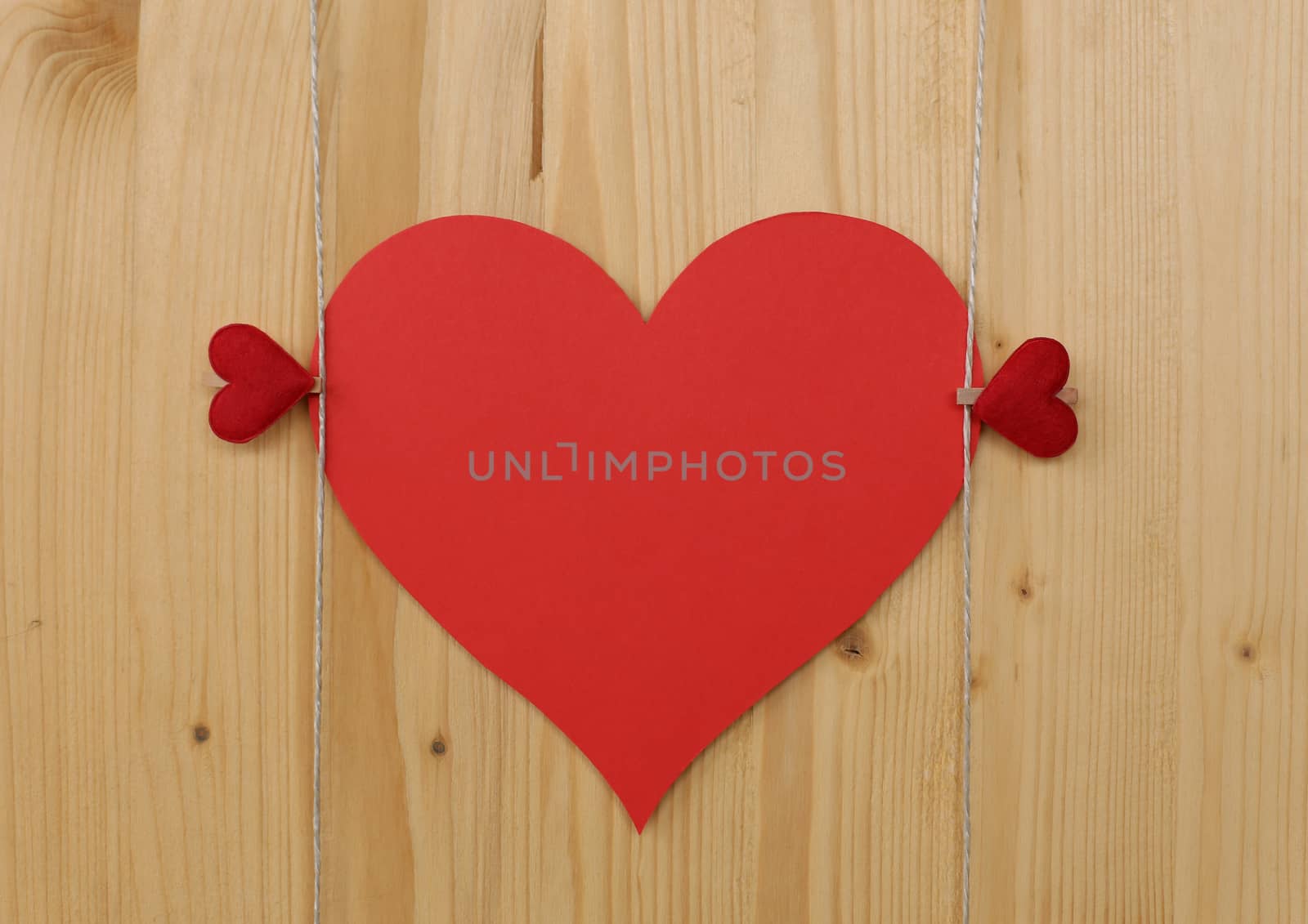 Two hearts with clothes pegs and red paper heart on a cord on wood