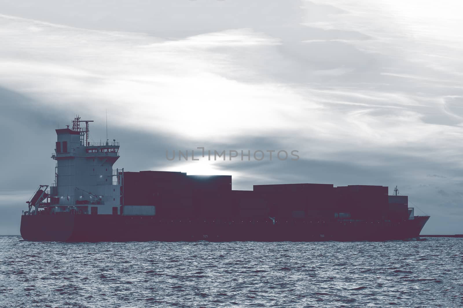 Full container ship leaving Riga city during hot sunset