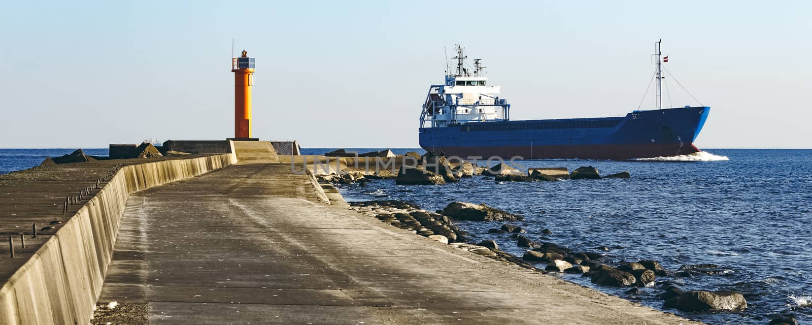 Blue cargo ship sailing against the breakwater dam