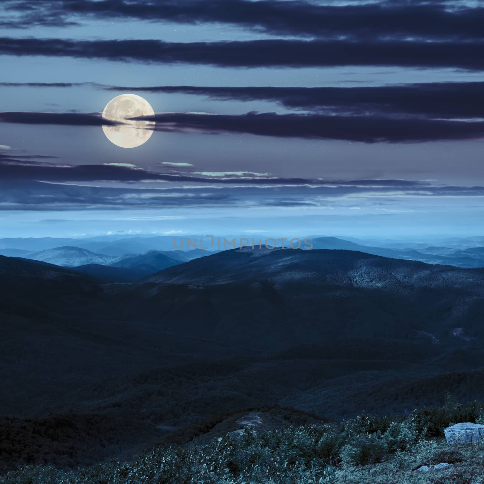 mountain landscape. valley with stones on the hillside. forest on the mountain under the beam of light falls on a clearing at the top of the hill at night in full moon light