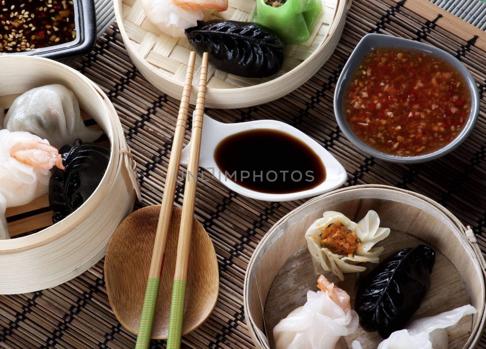 Various Dim Sum in Bamboo Steamed Bowls, Chili and Soy Sauces with Chopsticks closeup on Straw Mat background