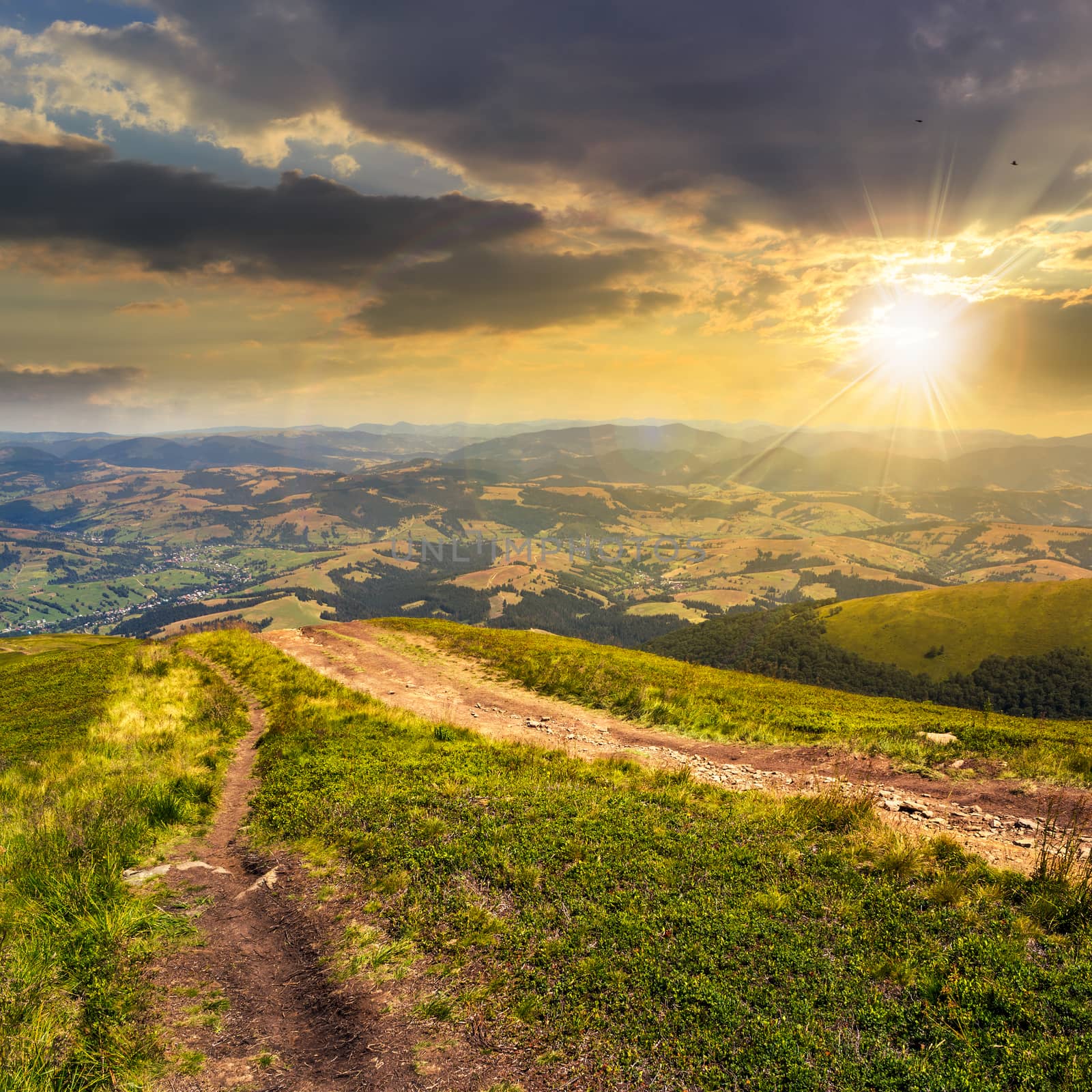 autumn landscape. path goes ftom the mountain range down to village in valley at the mountain foot at sunset