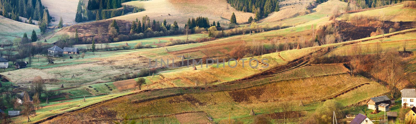Small village on alpine hills in spring. Spring panoramic landscape of sunny alpine morning. mountain village spring panorama. Beautiful rural scene. Village in the valley. Agricultural field on hillsides in mountains in morning light