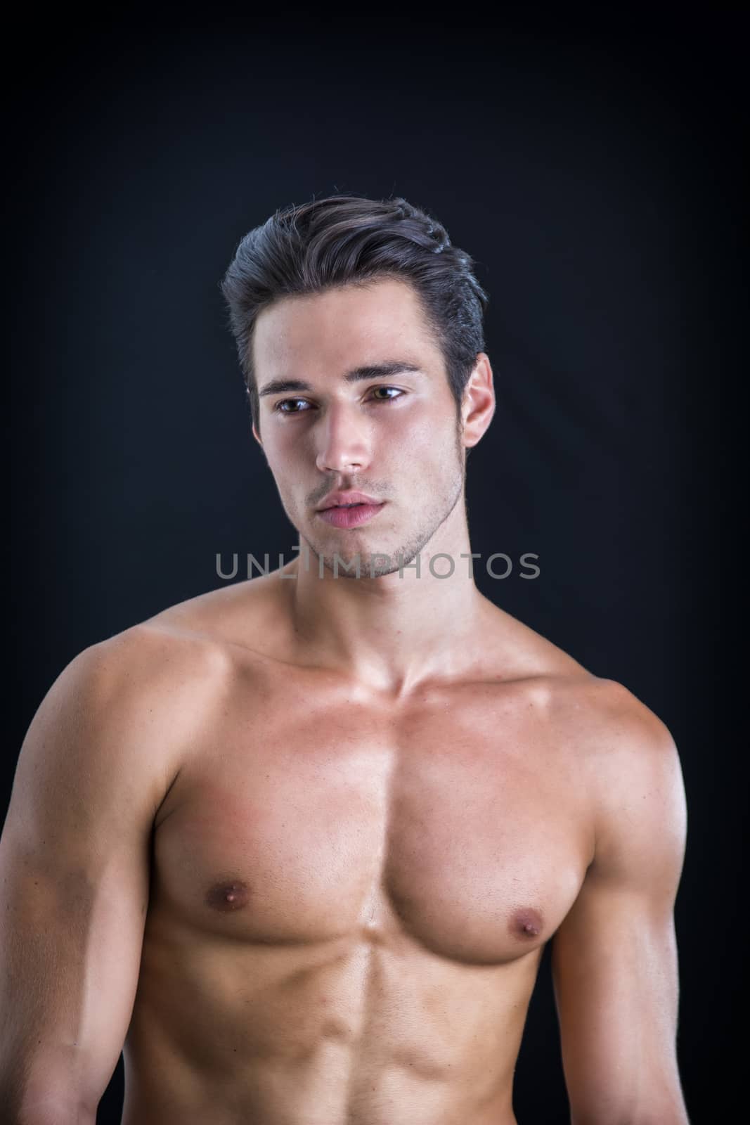 Handsome, fit young man wearing only underwear standing isolated on black background, looking at camera