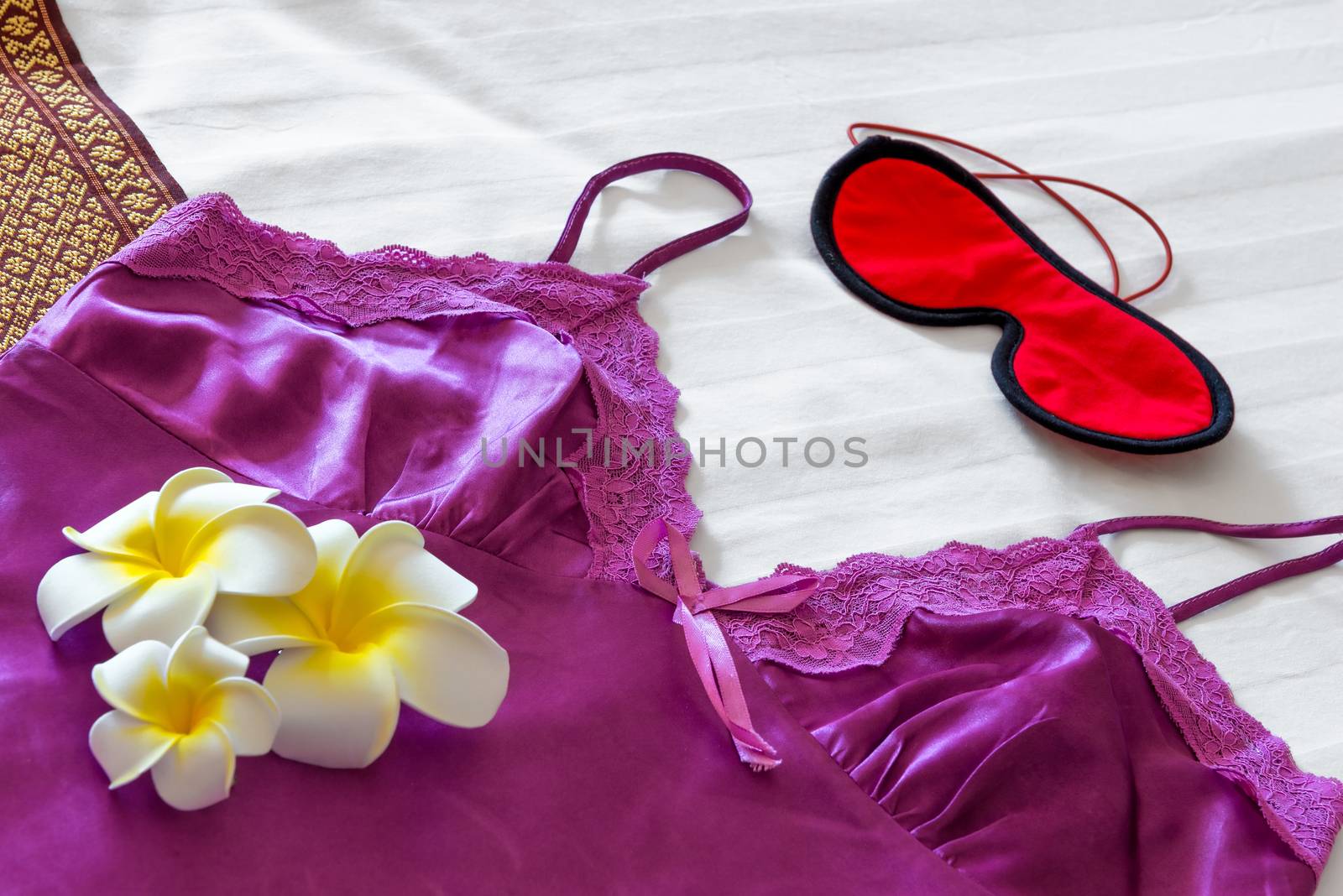 Silk pajamas, eye mask and frangipani on the bed close up