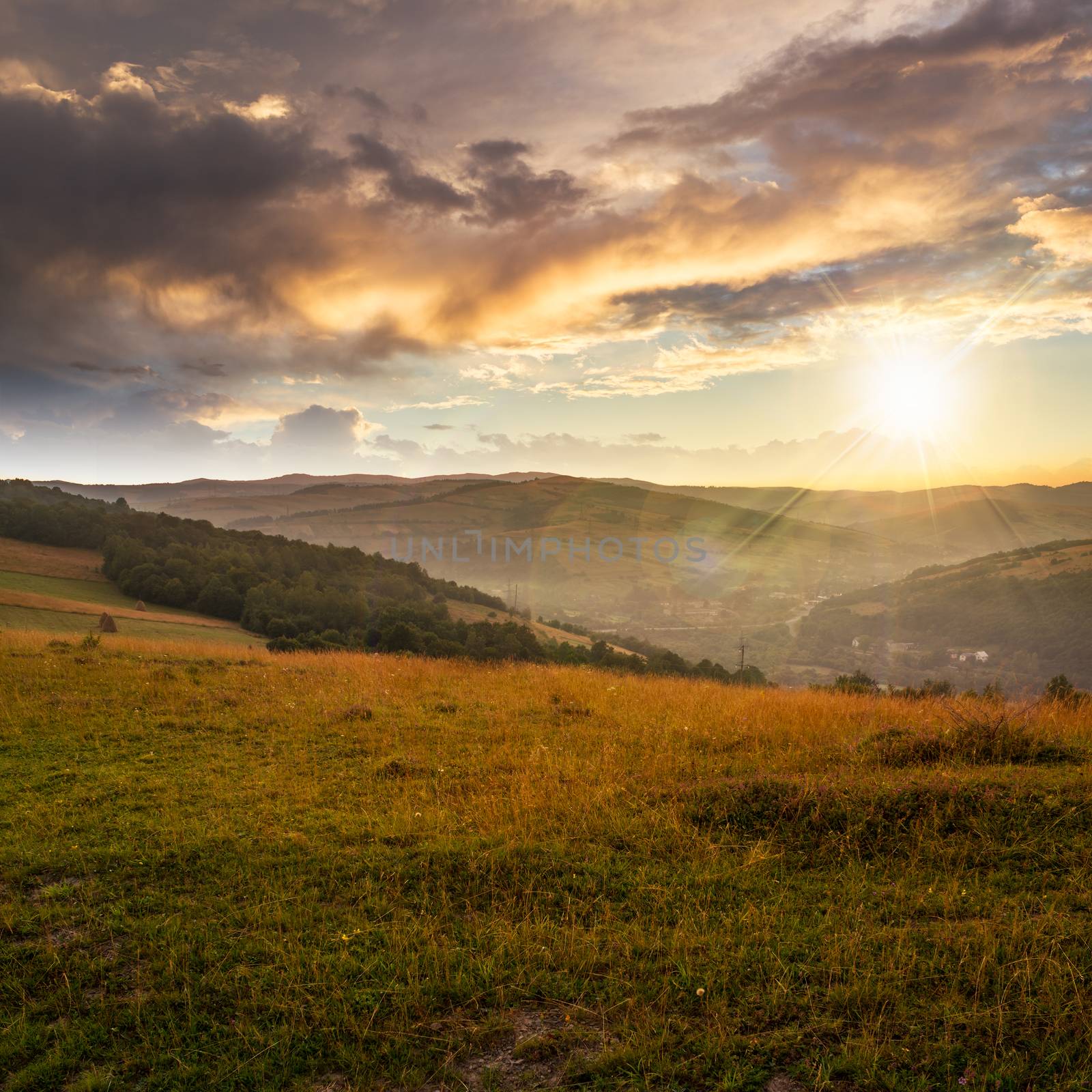 Stack of hay on a green meadow in the mountains in the morning under a blue summer sky at sunset