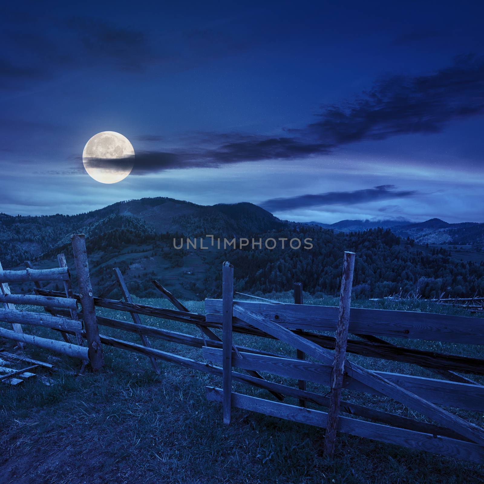 autumn landscape. fence near the meadow path on the hillside. forest in fog on the mountain. at night in full moon light