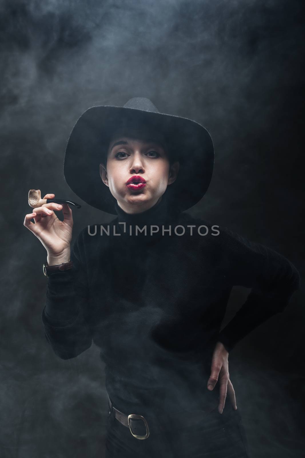 girl in black holding a pipe and blowing the smoke towards camera