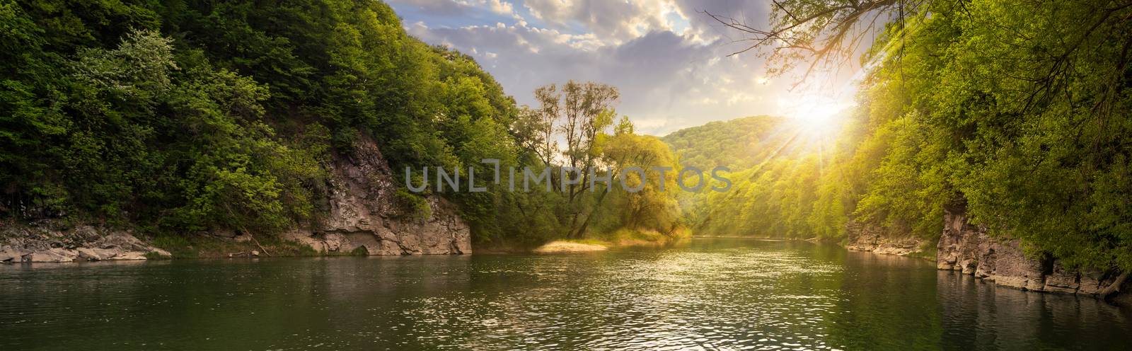 mountain river with stones on the shore in the forest near the mountain slope in sunset light