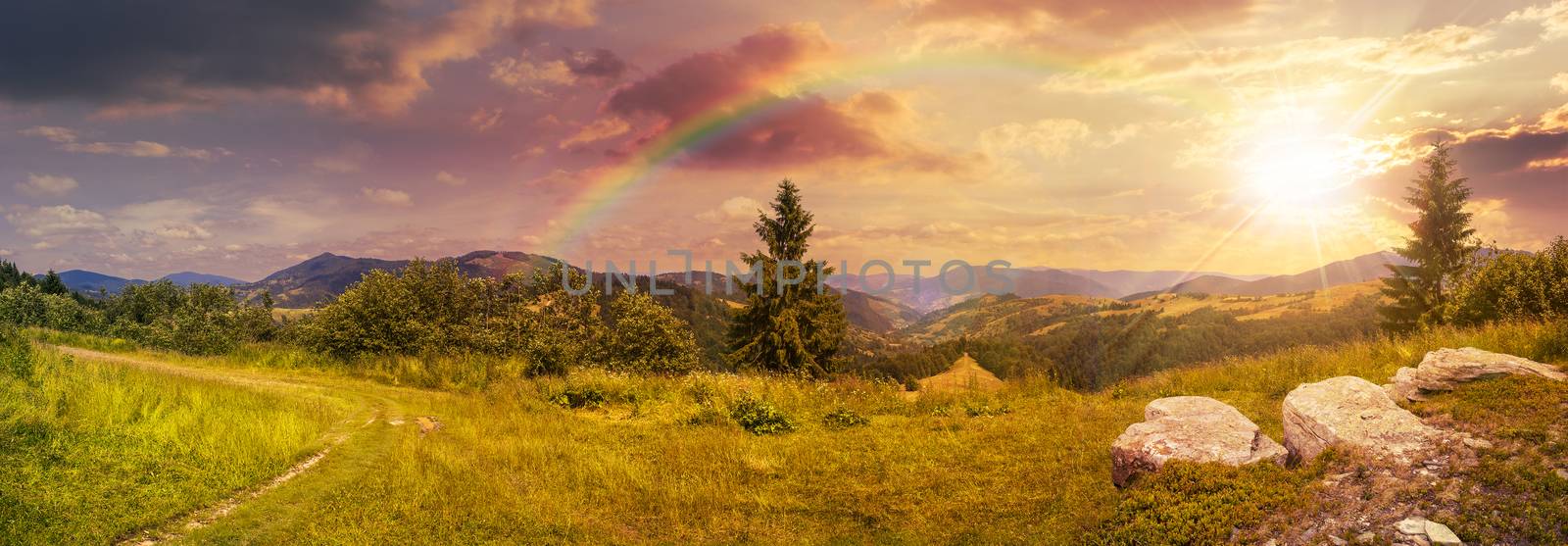 boulders on hillside meadow in mountain at sunset with rainbow by Pellinni