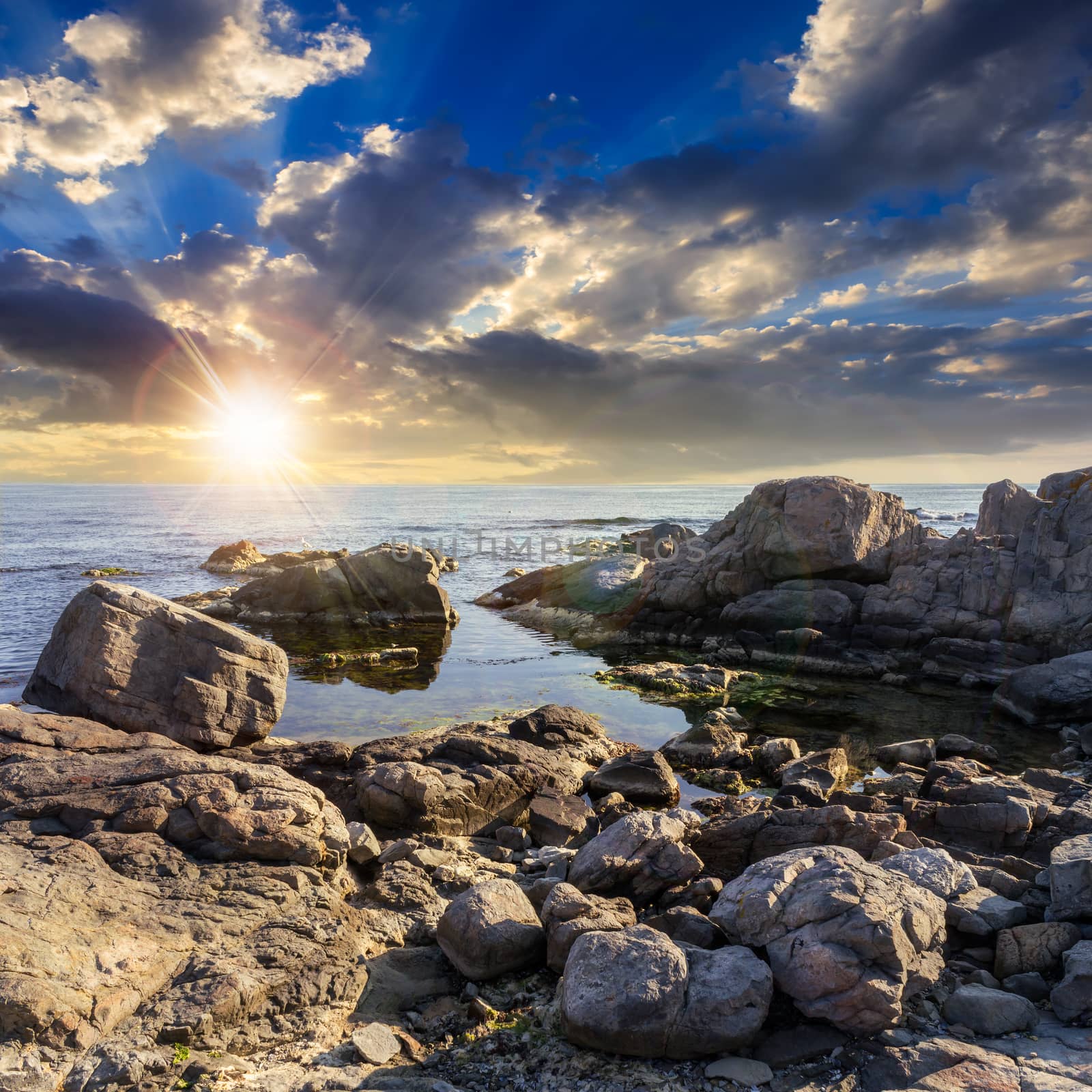calm sea wave on rocky shore with boulders at sunset