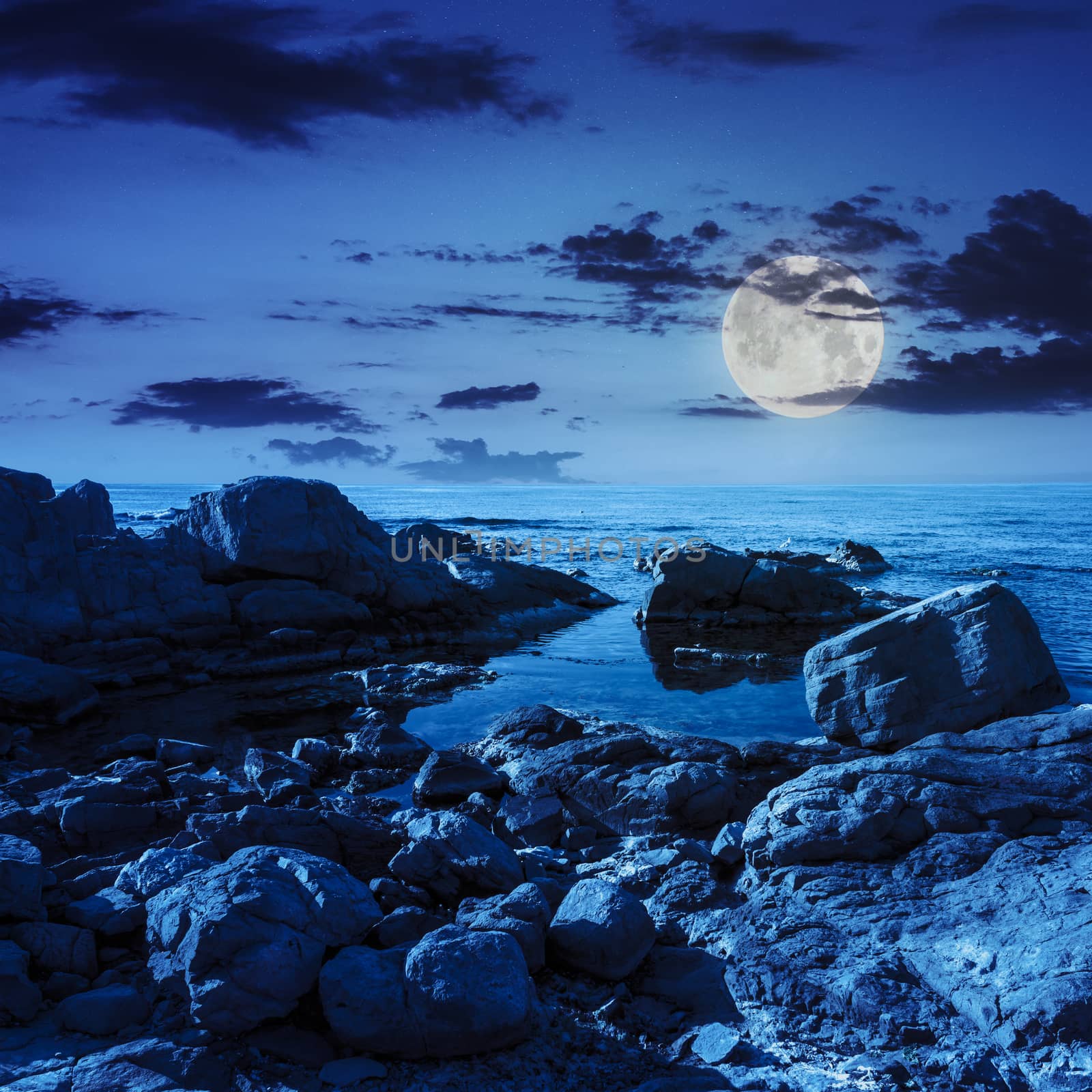 calm sea wave on rocky shore with boulders at night in moon light