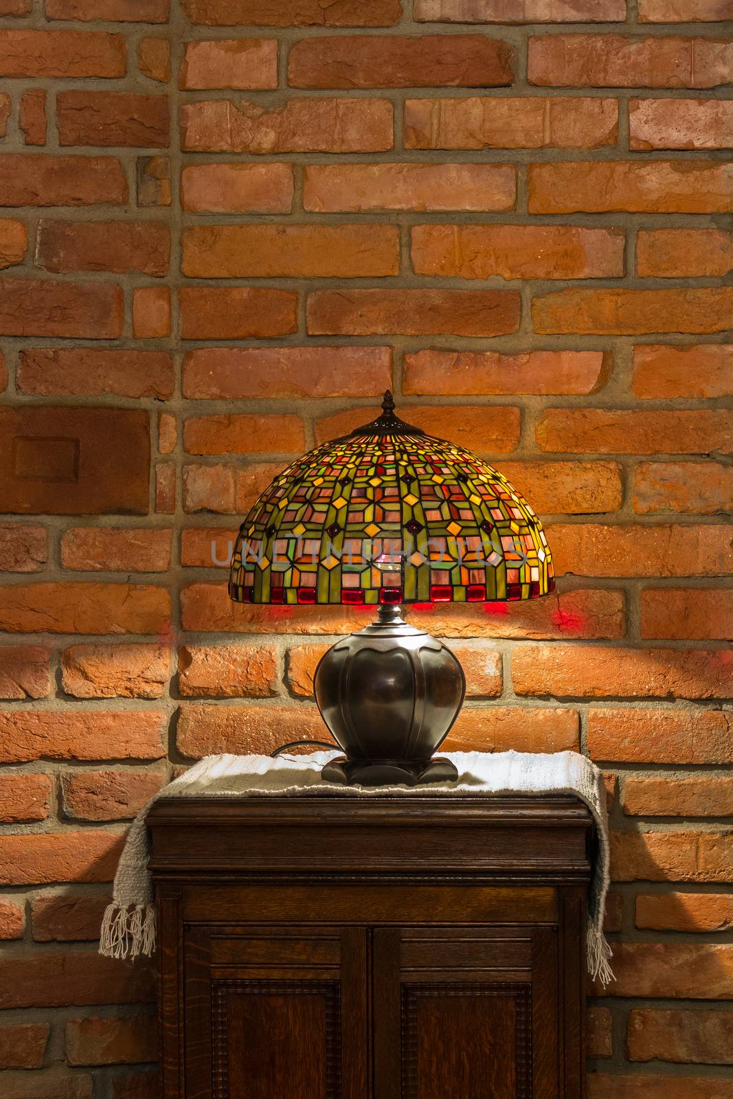 table lamp of stained-glass on old wooden stand on red brick wall background
