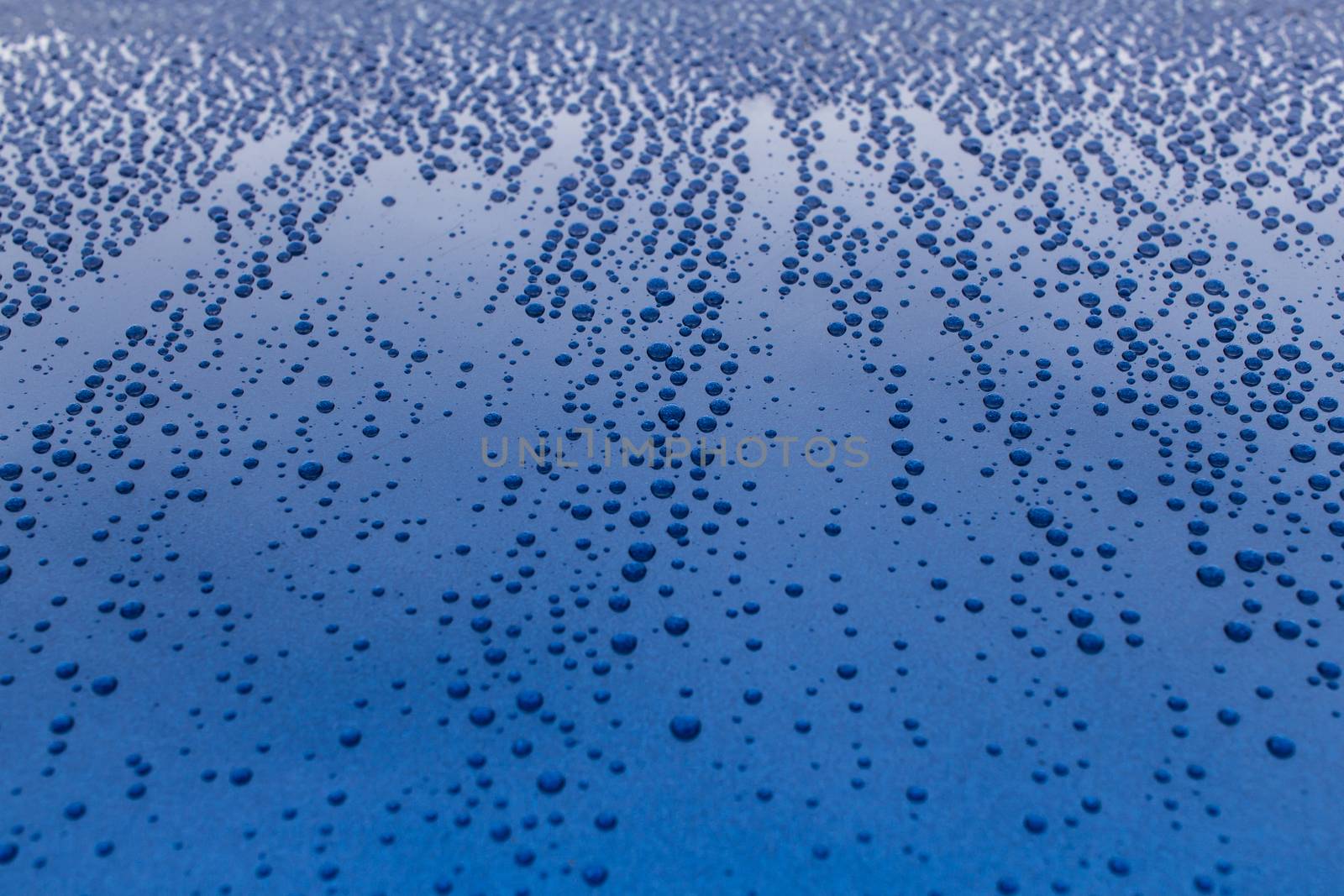 Many drops of water on a blue surface. Traces of rain on the hood of the car.