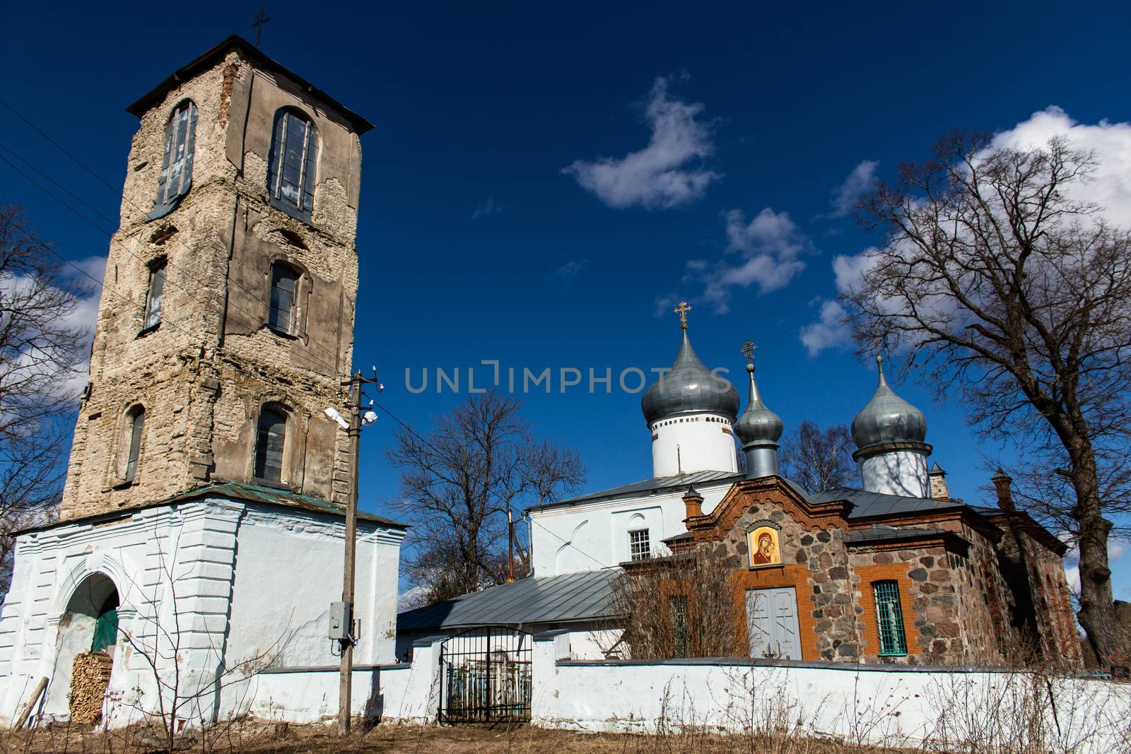 Orthodox Christian church next to the bell tower. Ancient buildings against a blue sky with white clouds. Sunny spring day. Deepest feeling of peace and tranquility.