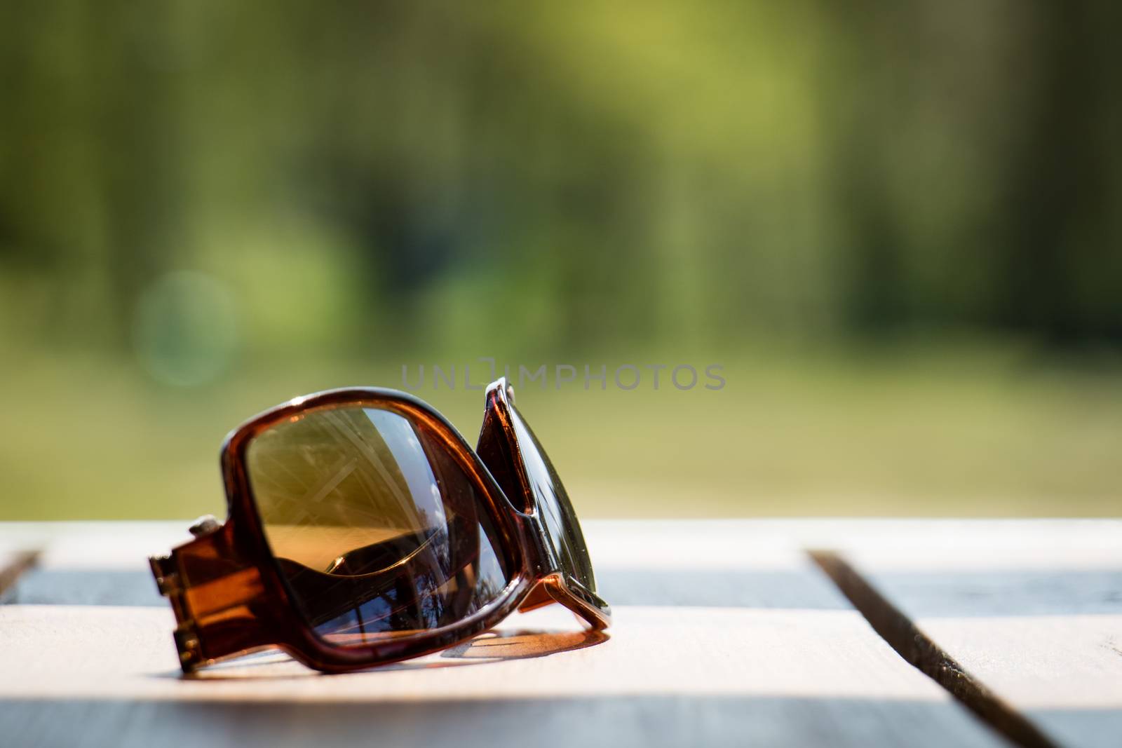 Sunglasses on the table in the sun on a wooden table by wytrazek