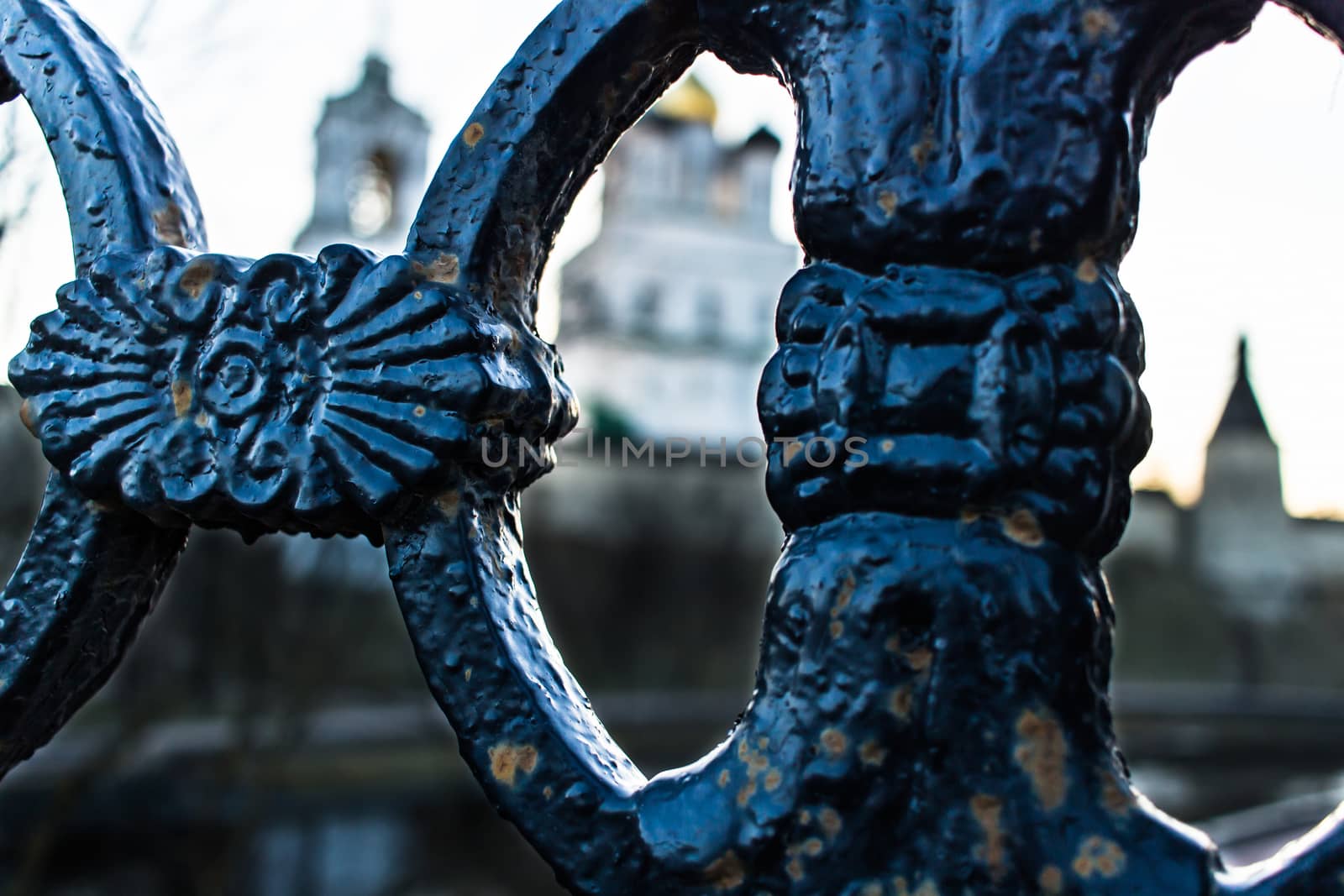 A fragment of cast-iron fencing against the background of an ancient fortress and a cathedral of the Holy Trinity.