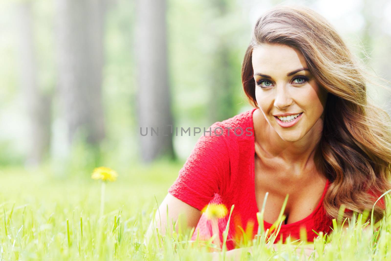 Beautiful young woman in red dress lying on grass