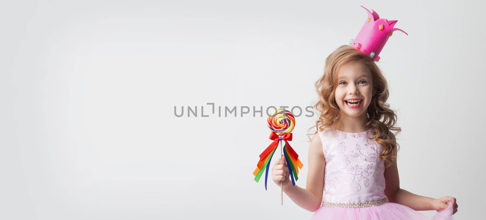 Small princess girl in crown holds a large spiral decorated lollipop candy