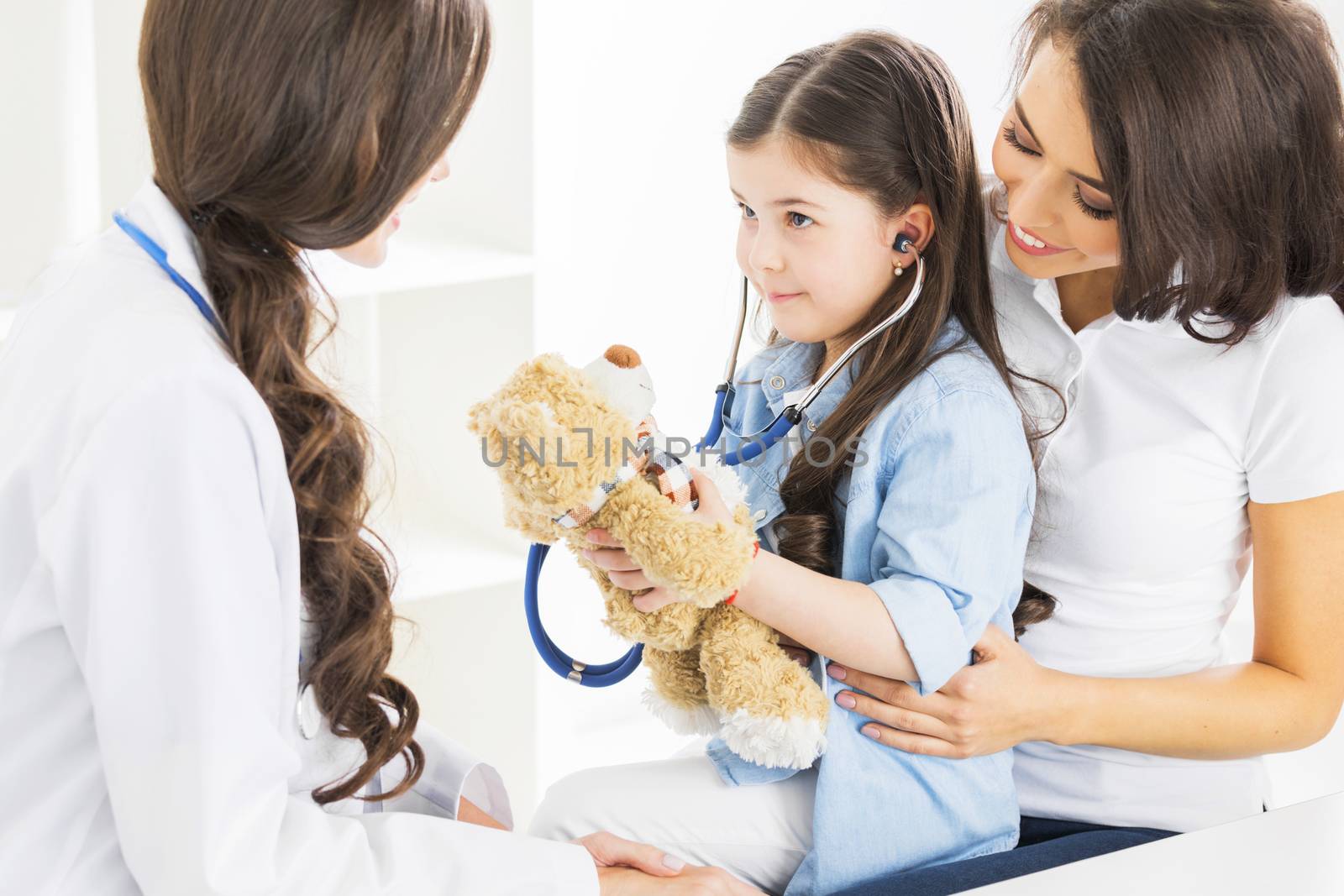 Mother and daughter at pediatrician office, girl examinate heart beat of teddy bear with stethoscope