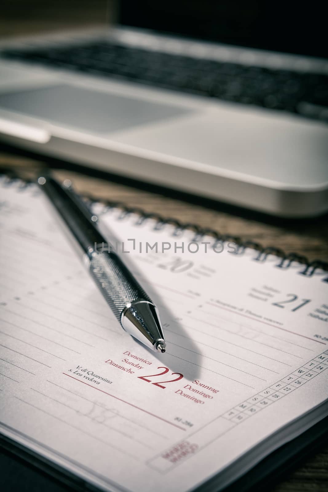 Closeup of a pen over a planner with a laptop on background