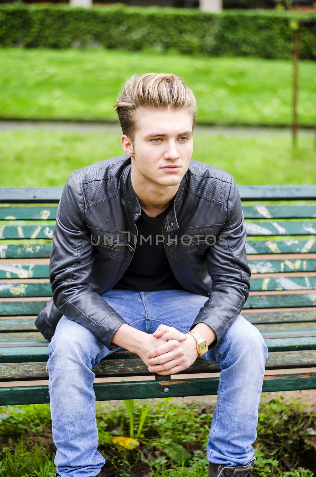 Handsome blond young man sitting on green, wooden park bench