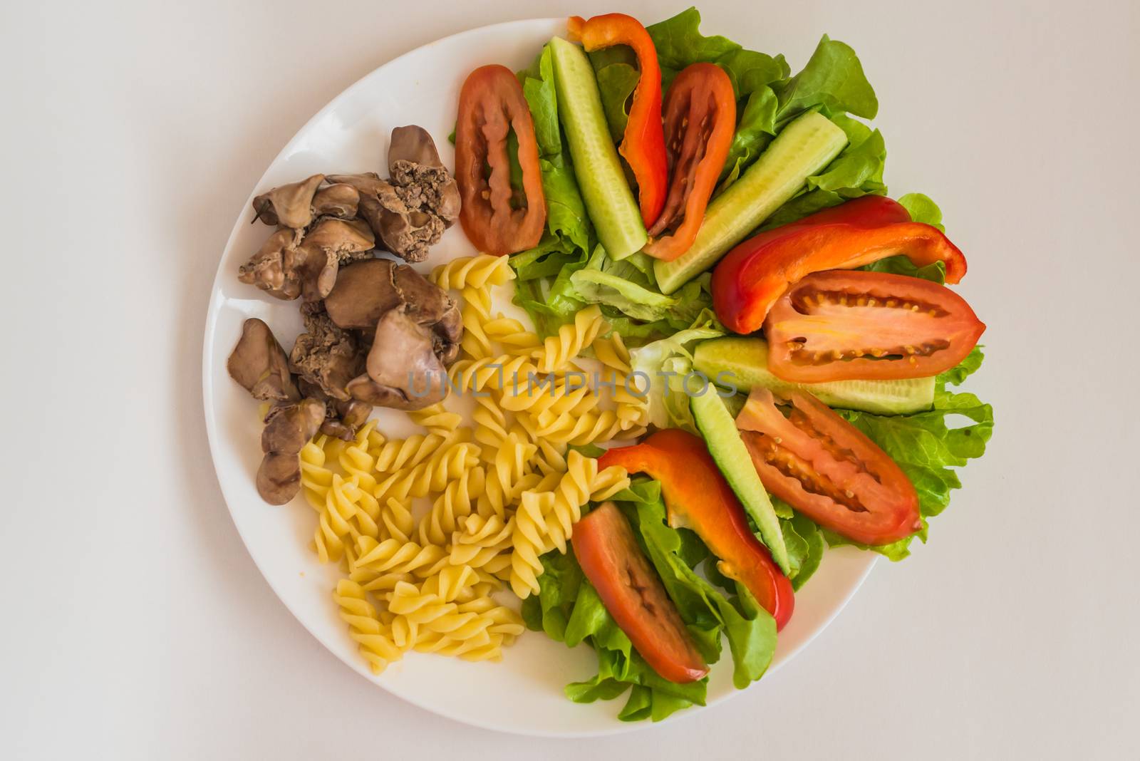 sliced tomatoes, cucumbers, lettuce, boiled pasta and fried chicken liver in the white plate on a white background