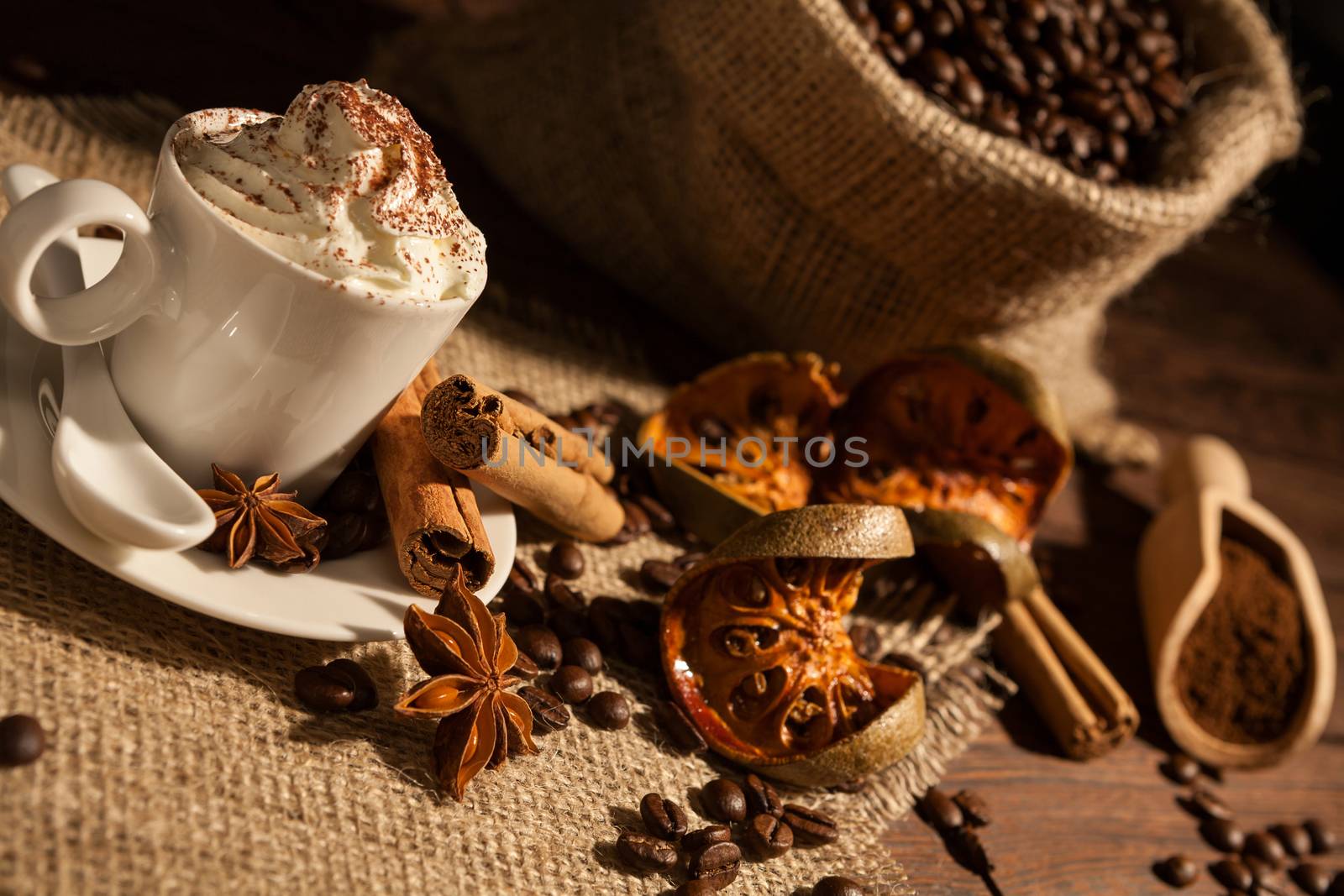 Close-up of a cup of coffee with whipped cream, cocoa powder, star anise, cinnamon and dried orange fruit