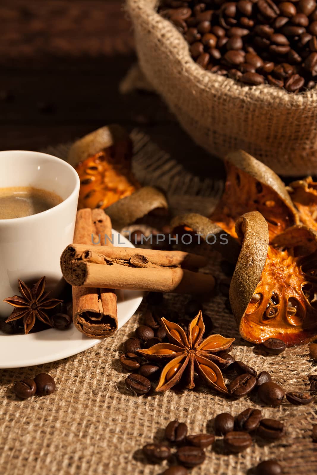 Close-up of coffee cup with cinnamon, star anise, dried orange fruit and a coffee sack on background
