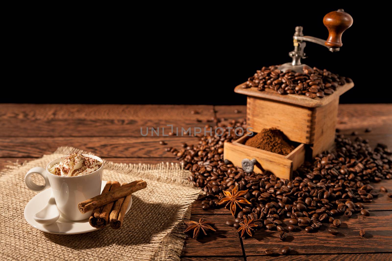 Coffee cup with whipped cream and coffee grinder over a wooden background