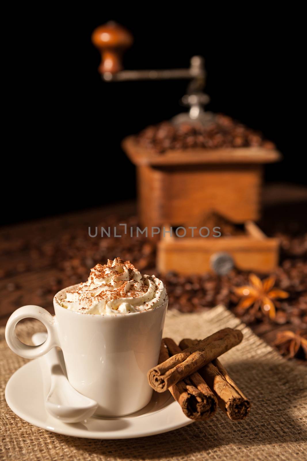 Coffee cup with whipped cream and cocoa powder and coffee grinder on background