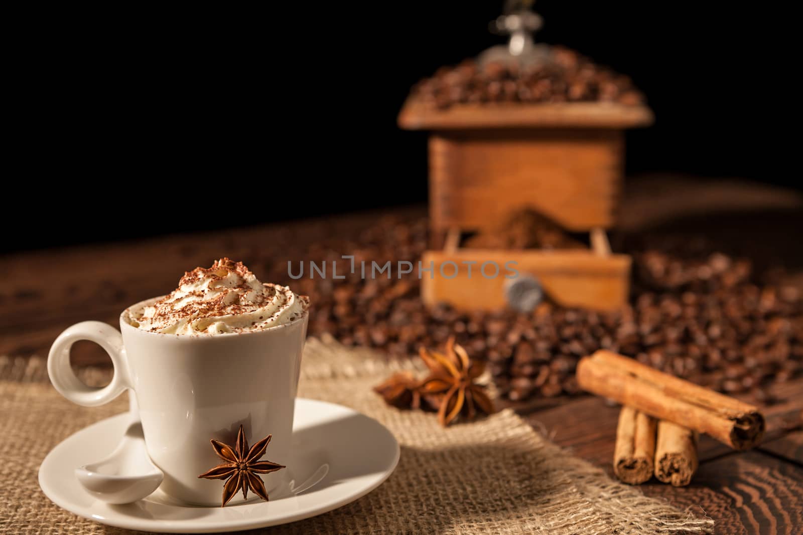 Coffee cup with whipped cream, cocoa powder and star anise with coffee grinder on background